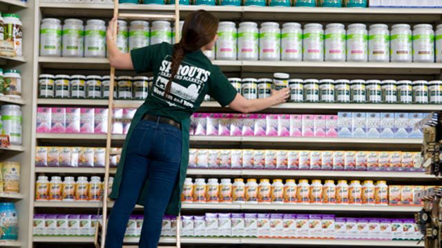 A Sprouts employee on a ladder stocks a shelf.