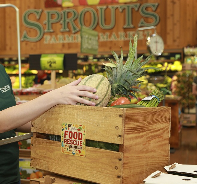 A person placing a cantaloupe in a wooden crate in a grocery store.