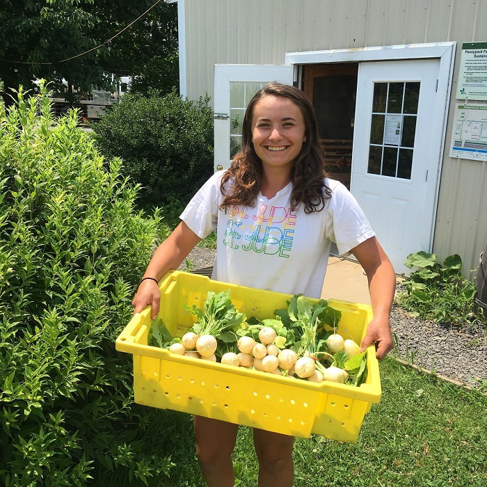 Girl smiles with large bin of produce