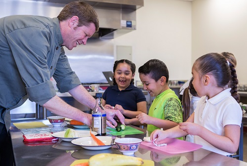 A chef helps young students prepare ingredients.