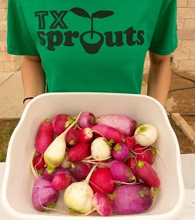 A girl holds a bowl of root vegetables.