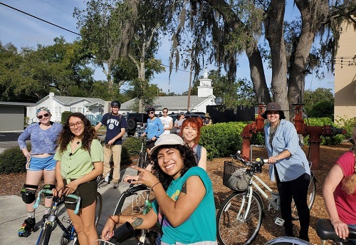 A group of bicyclists smile on a street corner. 
