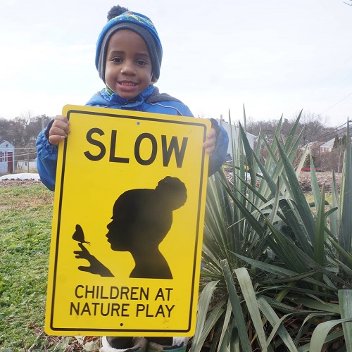 A young boy holds a sign reading "Children at nature play"