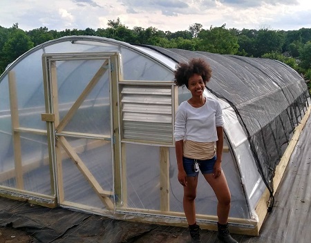 Backyard Basecamp Founder, Atiya Wells, stands next to the hoop house on site.