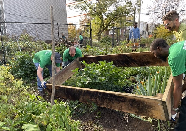 Volunteers place a wooden garden bed into a vibrant garden.